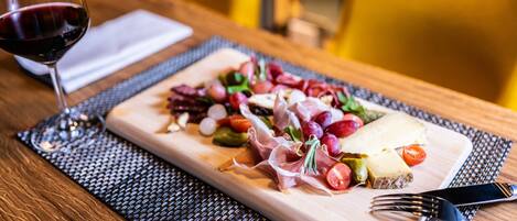 Una mesa de madera con una tabla de embutidos, una copa de vino tinto y un tenedor.