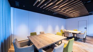 Una sala de conferencias moderna con mesas y sillas de madera, un diseño de techo con listones y un ventanal con cortinas.