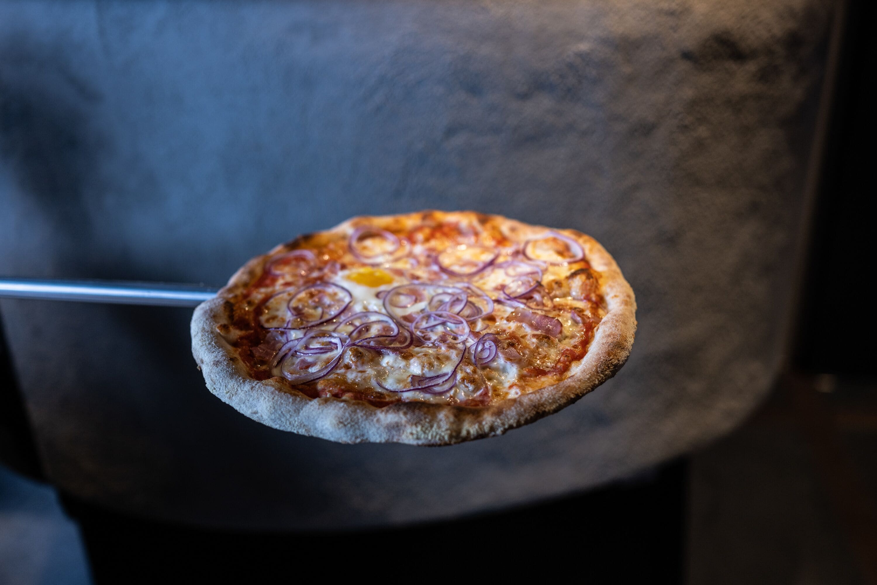 Une pizza garnie, maintenue par un ustensile en métal.
