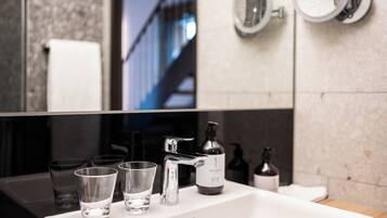 A bathroom with a white sink, two mirrors, and a large mirror above the sink. There are four clear glasses on the sink, a bottle of hand soap, and a bottle of lotion.
