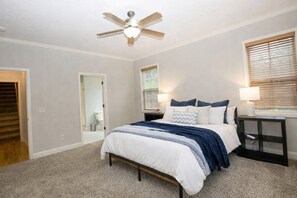 A bedroom with a bed, a ceiling fan, a nightstand, and a window with blinds. - A Pinehurst Getaway – Games, Golf & More! - 4BR/3BA Sleeps 8 (Pinehurst)
