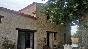 Un bâtiment rustique en pierre, doté d’une terrasse en gravier, de sièges extérieurs et d’un arbre qui offre de l’ombre.