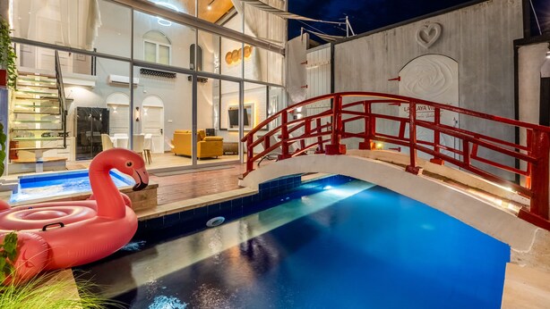 Un hotel moderno con fachada de vidrio, piscina y un puente rojo.