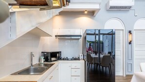 Cocina compacta con lavamanos, estufa y microondas. Cuenta con muebles blancos, encimera de madera y un comedor con sillas y mesa.