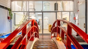 Un edificio moderno con fachada de vidrio, un puente metálico rojo y un piso con diseño que conduce a una puerta.
