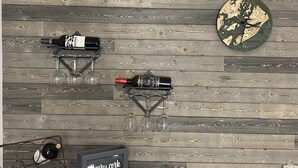 Una pared con diseño de tablones de madera, un botellero con botellas y copas, y un cartel enmarcado que dice 