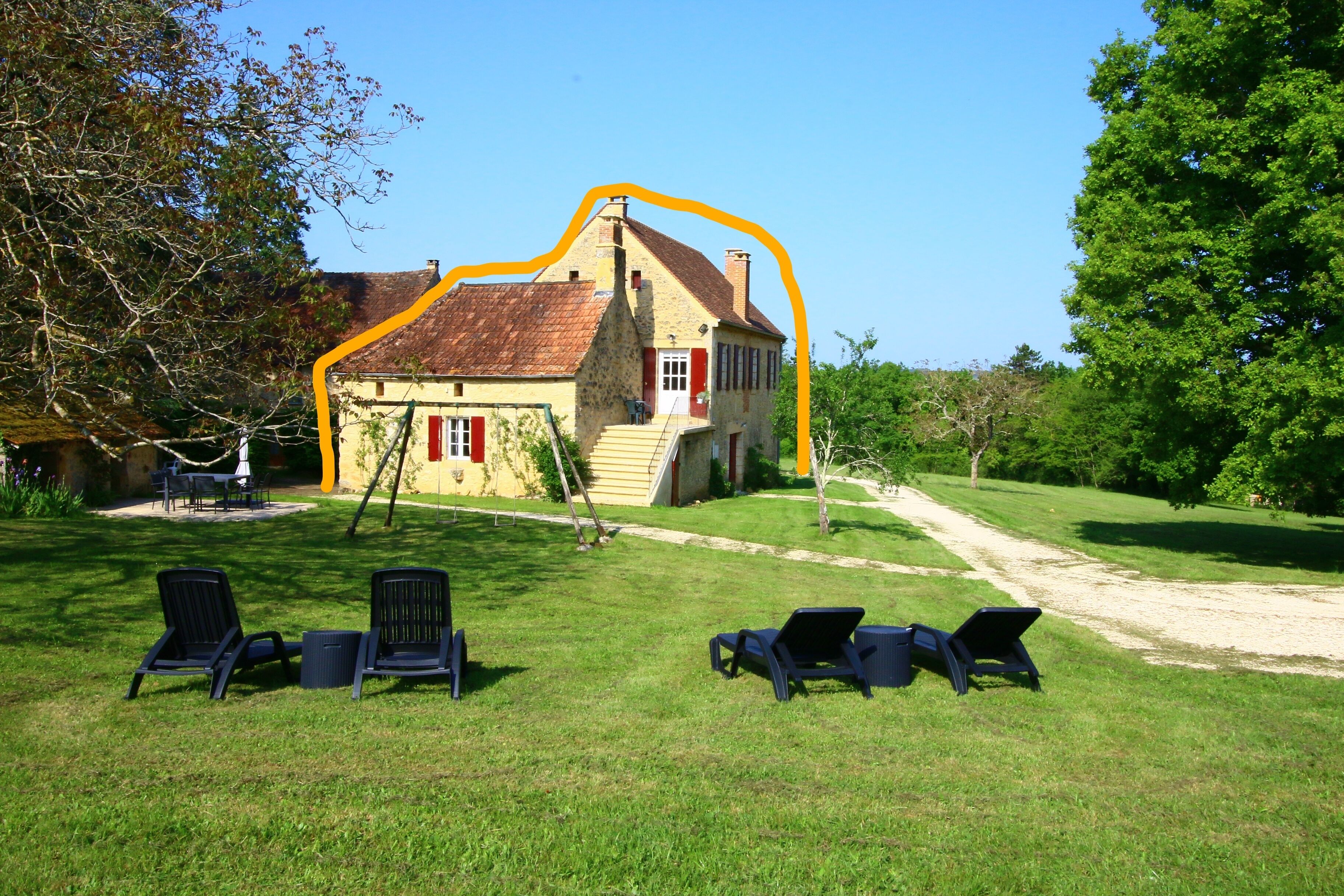 Ein Haus mit rotem Dach, einer Stein-Fassade und einer Veranda mit Stühlen.