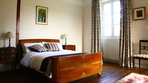 Un dormitorio con una cama de madera, dos mesitas de noche con lámparas, una ventana con cortinas y una silla.