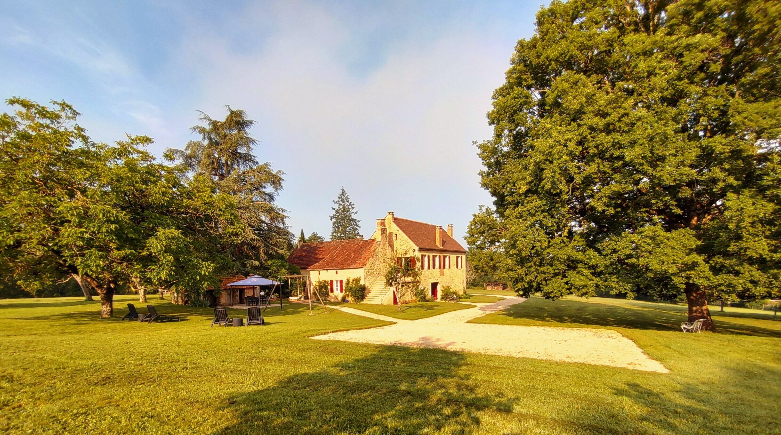 A large stone building with a red roof, surrounded by lush green trees and a well-maintained lawn.