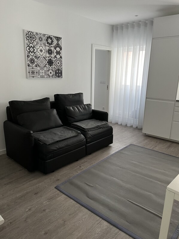 Ein modernes Wohnzimmer mit einem schwarzen Ledersofa, einem grauen Teppich und einer weißen Kommode.