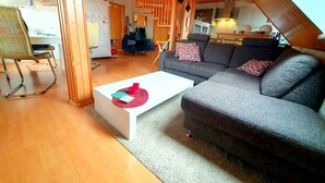 Un espace de vie chaleureux de style loft, avec un canapé gris, une table basse blanche et un plafond en bois.