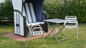 Un espace patio comprenant une table en métal et deux chaises, un banc rembourré et un petit coin salon abrité.