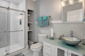 Un baño con un lavabo de vidrio, un inodoro y una zona de ducha.