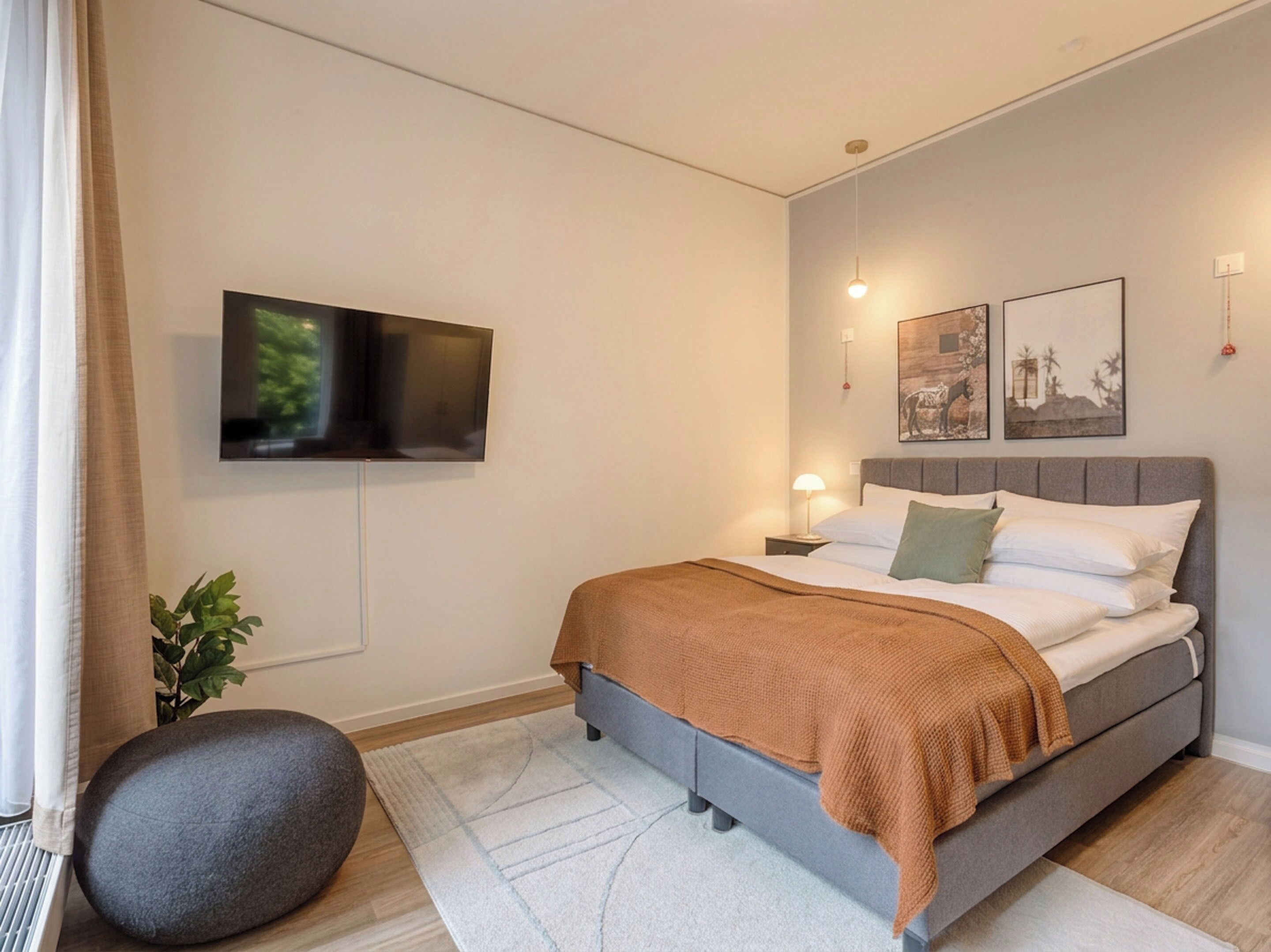 A modern bedroom with a bed, a flat-screen TV, a bedside lamp, and artwork on the wall.