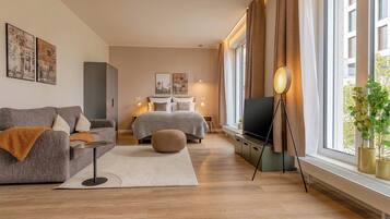 Ett modernt sovrum med en soffa, en säng, en tv och ett stort fönster med gardiner.