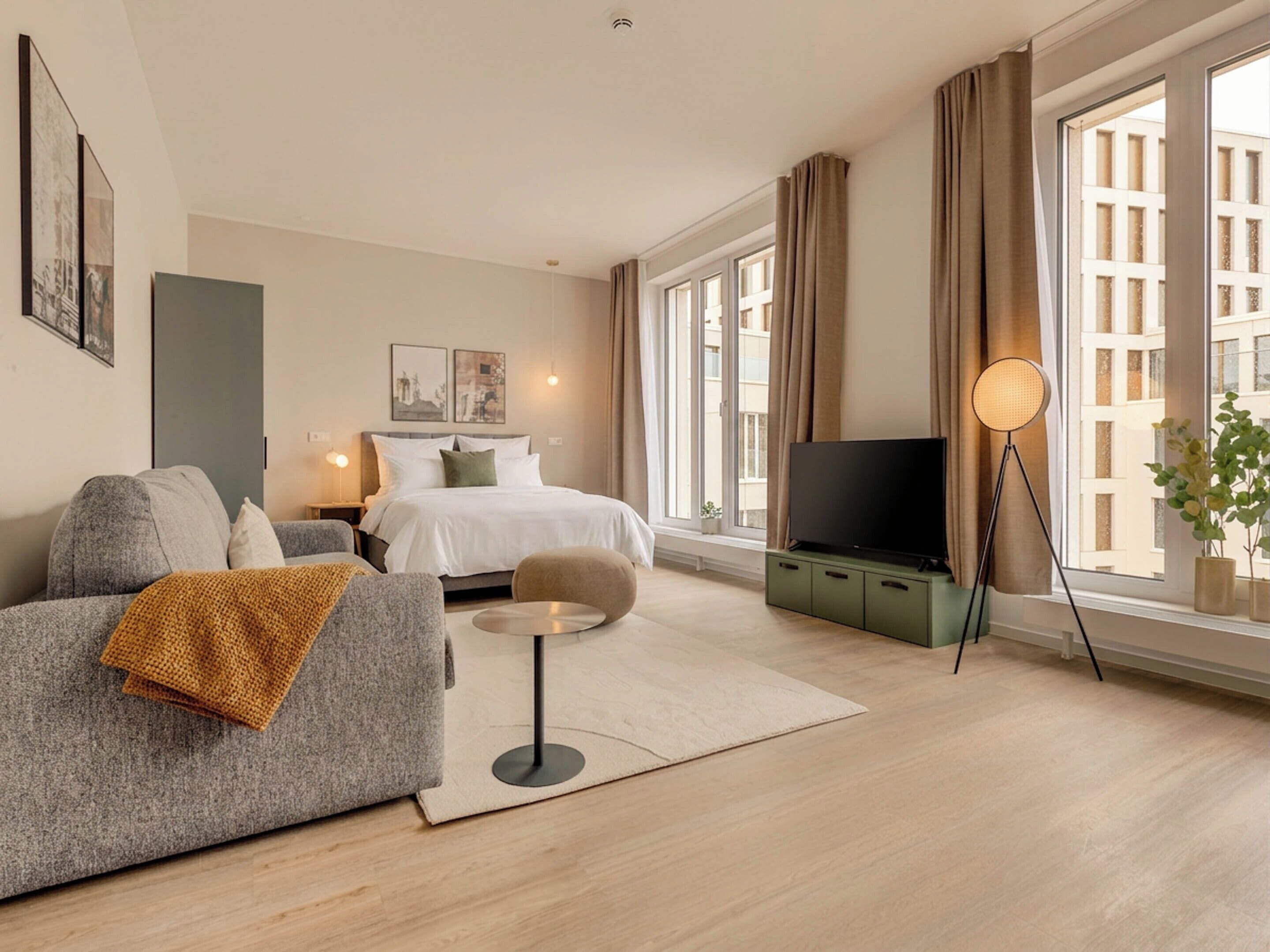 A modern hotel room with a bed, sofa, TV, and large windows.