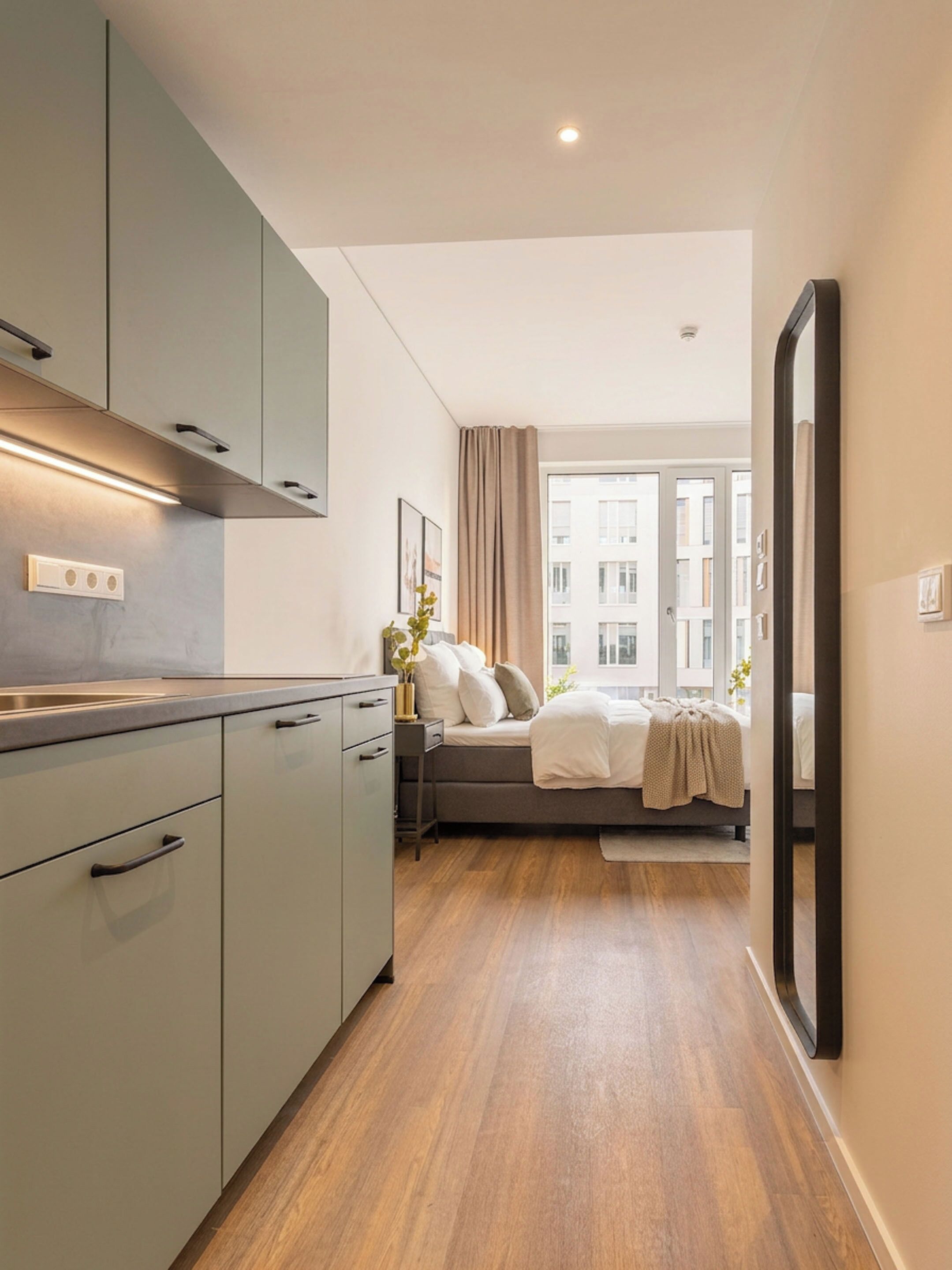 A modern hotel room with a kitchenette, a bed with a view, and a large mirror.