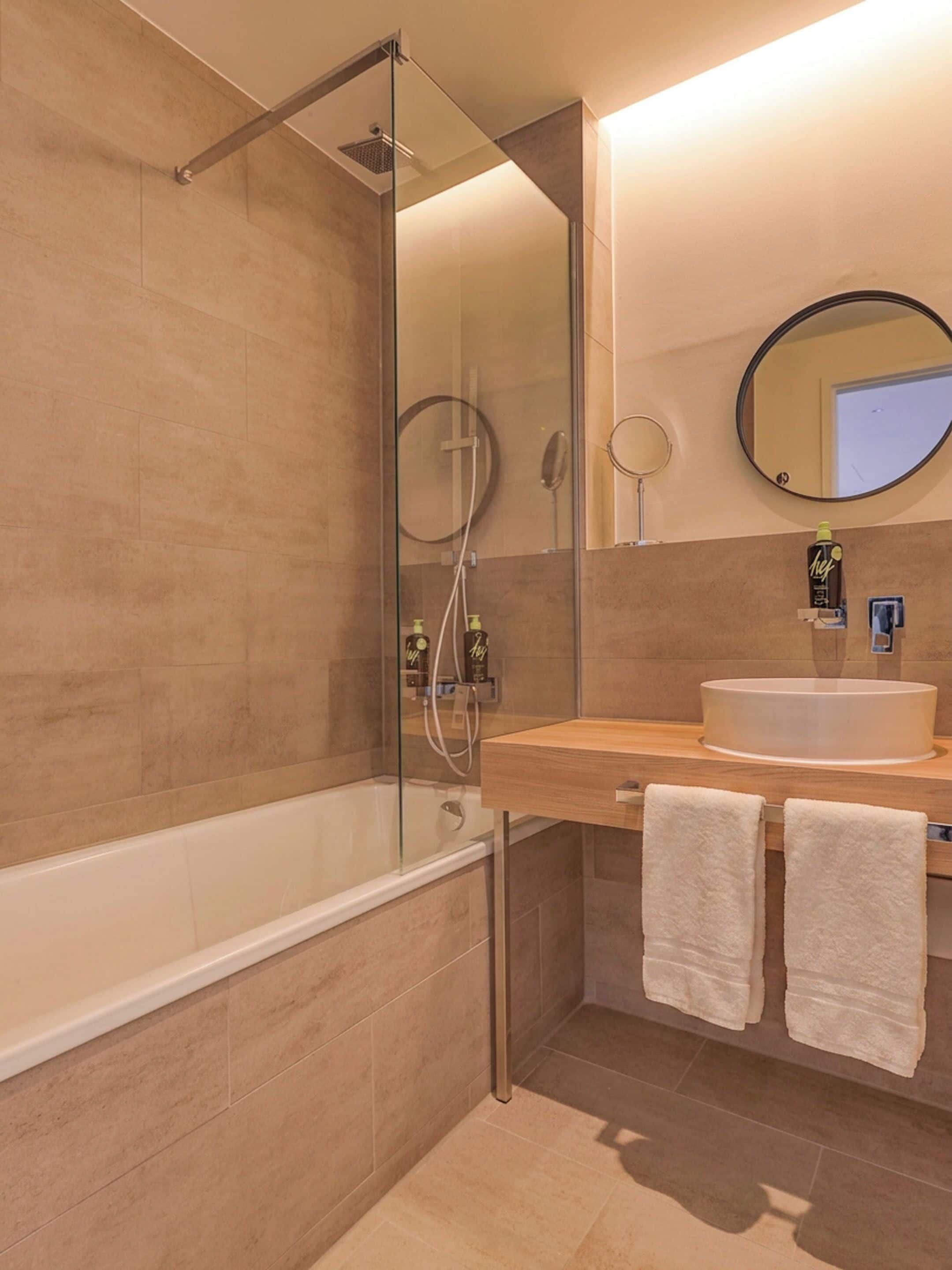 Une salle de bain moderne avec une douche à parois de verre, une baignoire, un lavabo avec un miroir et deux serviettes.