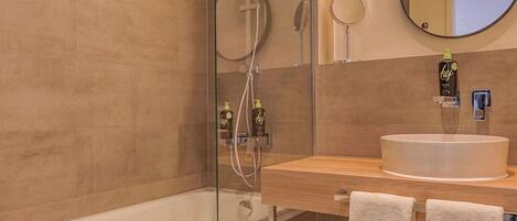 Une salle de bain moderne avec une douche à parois de verre, une baignoire, un lavabo avec un miroir et deux serviettes.