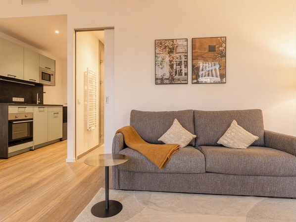 A modern living room with a grey sofa, a small round table, and a kitchen in the background. - Limehome Berlin Müllerstraße (Berlin)