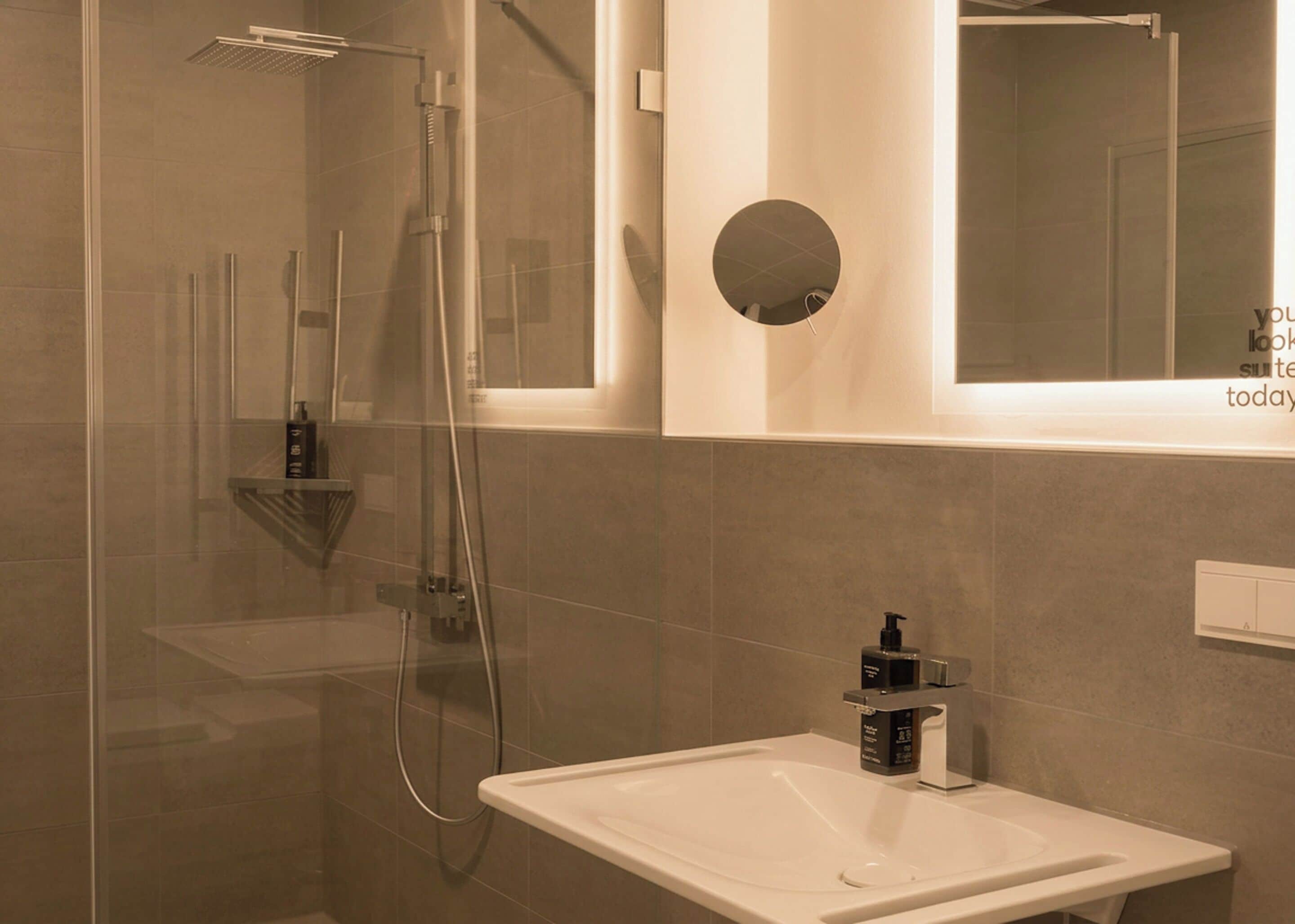 A modern bathroom with a glass-enclosed shower, a white sink, and a round mirror.