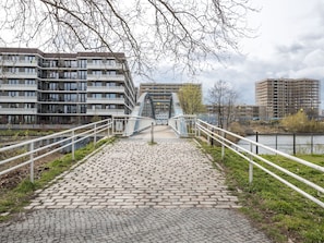 A cobblestone pathway leading to a modern bridge with a glass facade, flanked by white railings and overlooking a river.