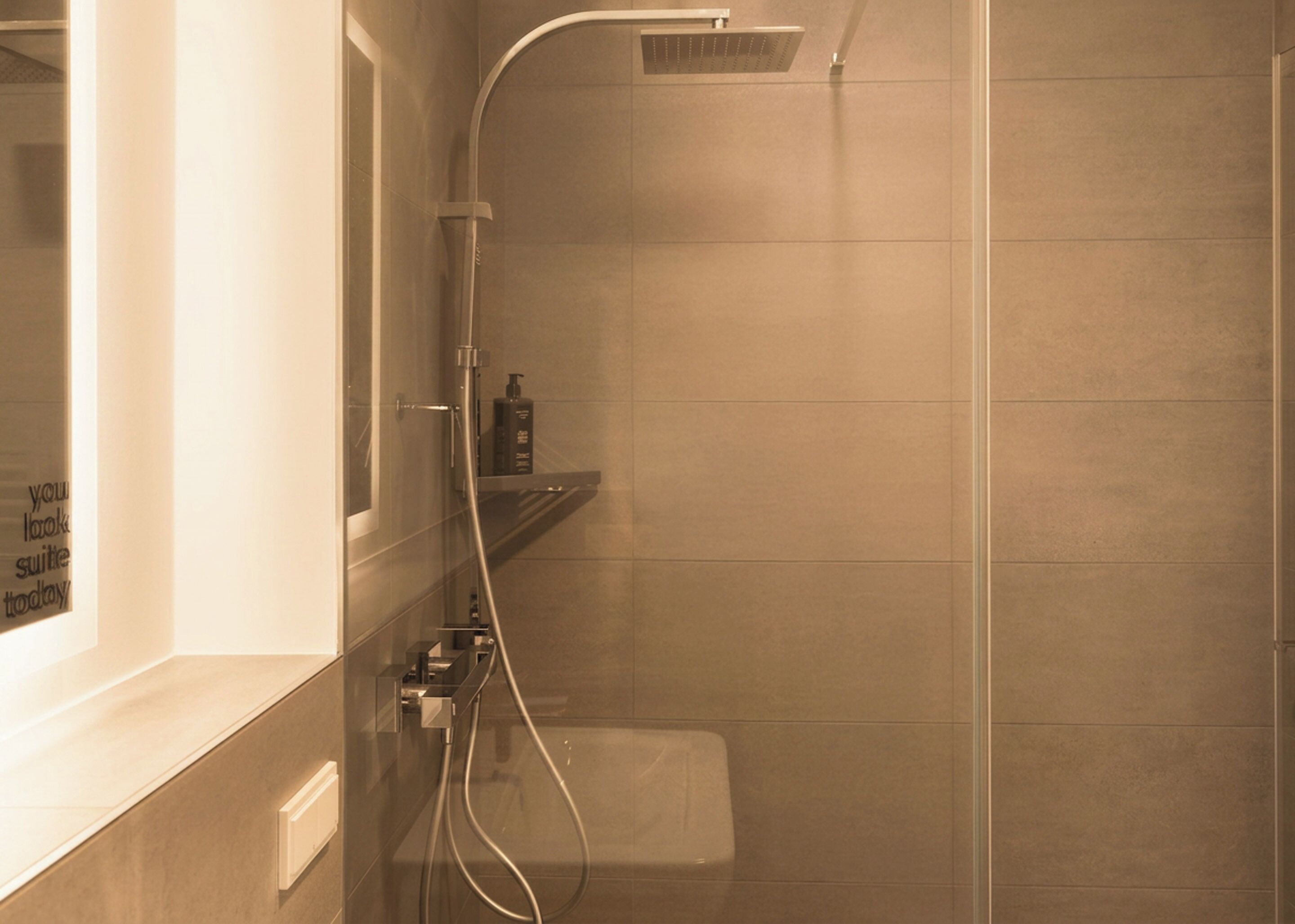 Een douche met een handdouche, een wandmengkraan en een klein plankje met toiletartikelen.