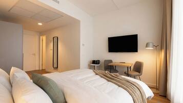 A hotel room with a bed, a desk, a chair, a flat-screen TV, a lamp, and a mirror.