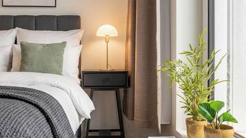 Une chambre à coucher moderne avec un lit, une table de chevet, une lampe, une fenêtre et des plantes en pot.