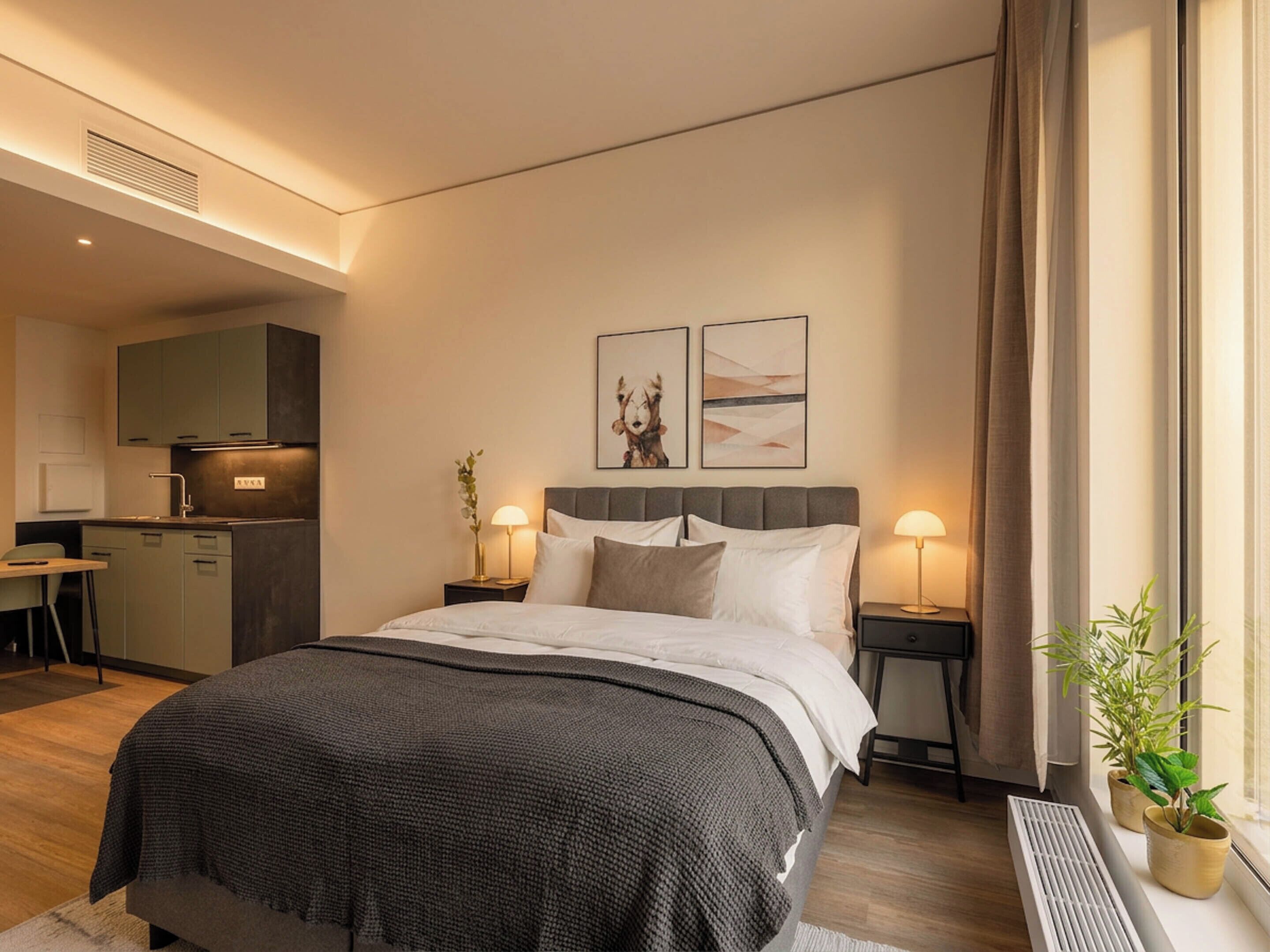 Una habitación de hotel moderna con cama, mesitas de noche, escritorio y kitchenette.