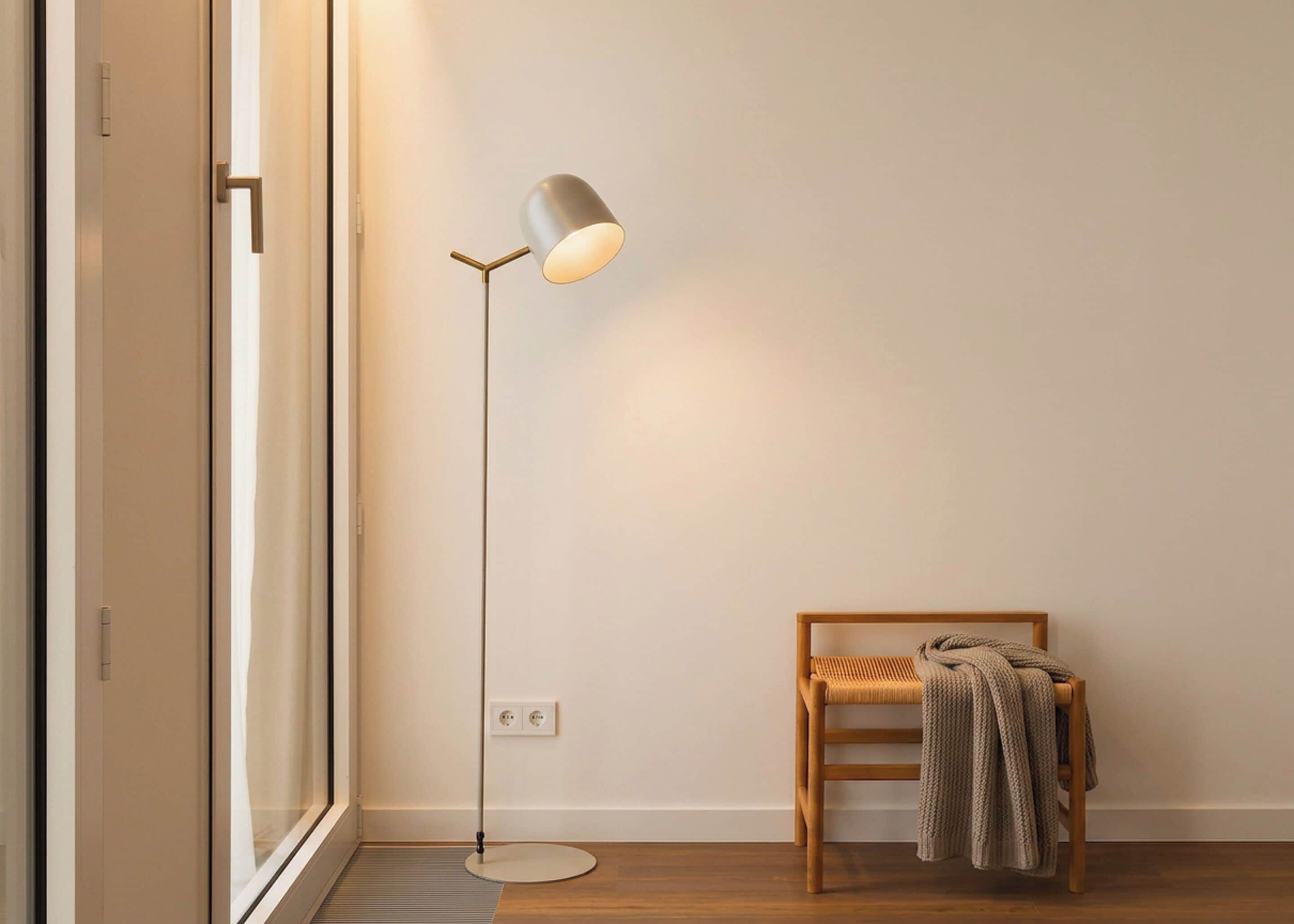 A modern room with a floor lamp, a wooden chair with a blanket, and a window with blinds.