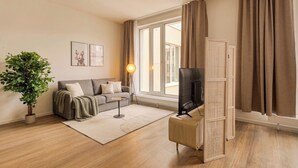 A modern living room with a sofa, a television, a floor lamp, and a potted plant. - Limehome Berlin Müllerstraße (Berlin)