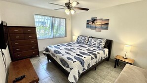 Un dormitorio con cama, cómoda, mesita de noche, ventilador de techo y ventana con persianas.