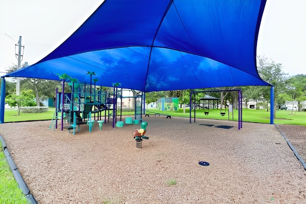 Un parque infantil con un toldo azul, estructuras de juego y superficie de goma.