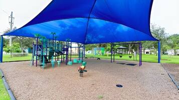 Un parque infantil con un toldo azul, estructuras de juego y superficie de goma.