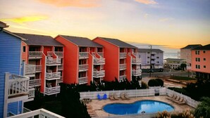 Un hôtel avec des bâtiments aux couleurs rouge et bleu, une piscine et une clôture blanche en bois.