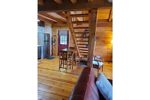 Interior de una cabaña de madera con cocina, comedor y escalera.