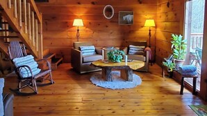 A wooden interior with a staircase, a round wooden table, two sofas, and a rocking chair. - Original Log Cabin, Private, Secluded, Mt views, Hot Tub, Honeymoon/Anniversary! (Gatlinburg)