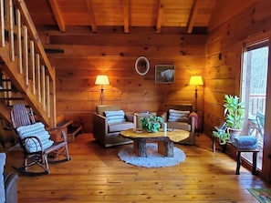 A wooden interior with a staircase, a round wooden table, two sofas, and a rocking chair. - Original Log Cabin, Private, Secluded, Mt views, Hot Tub, Honeymoon/Anniversary (Gatlinburg)