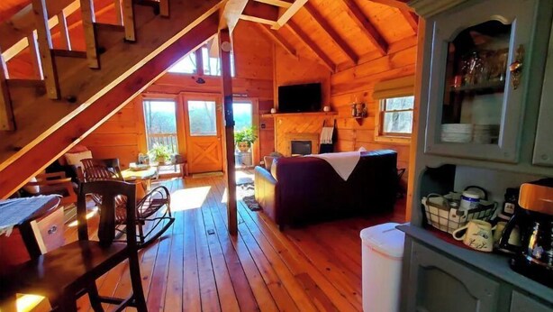 A cozy cabin with a wooden interior, a dining area, a sofa, and a kitchen area. - Original Log Cabin, Private, Secluded, Mt views, Hot Tub, Honeymoon/Anniversary! (Gatlinburg)