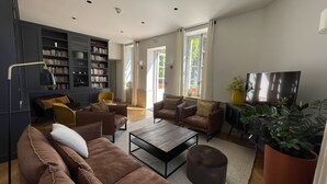 A modern living room with a sofa set, a coffee table, a bookshelf, and a television. - Manoir de Villamont (Savigny-les-Beaune)
