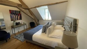 A bedroom with a sloped ceiling, a bed with white bedding, a bedside table, a lamp, and a painting on the wall. - Manoir de Villamont (Savigny-les-Beaune)
