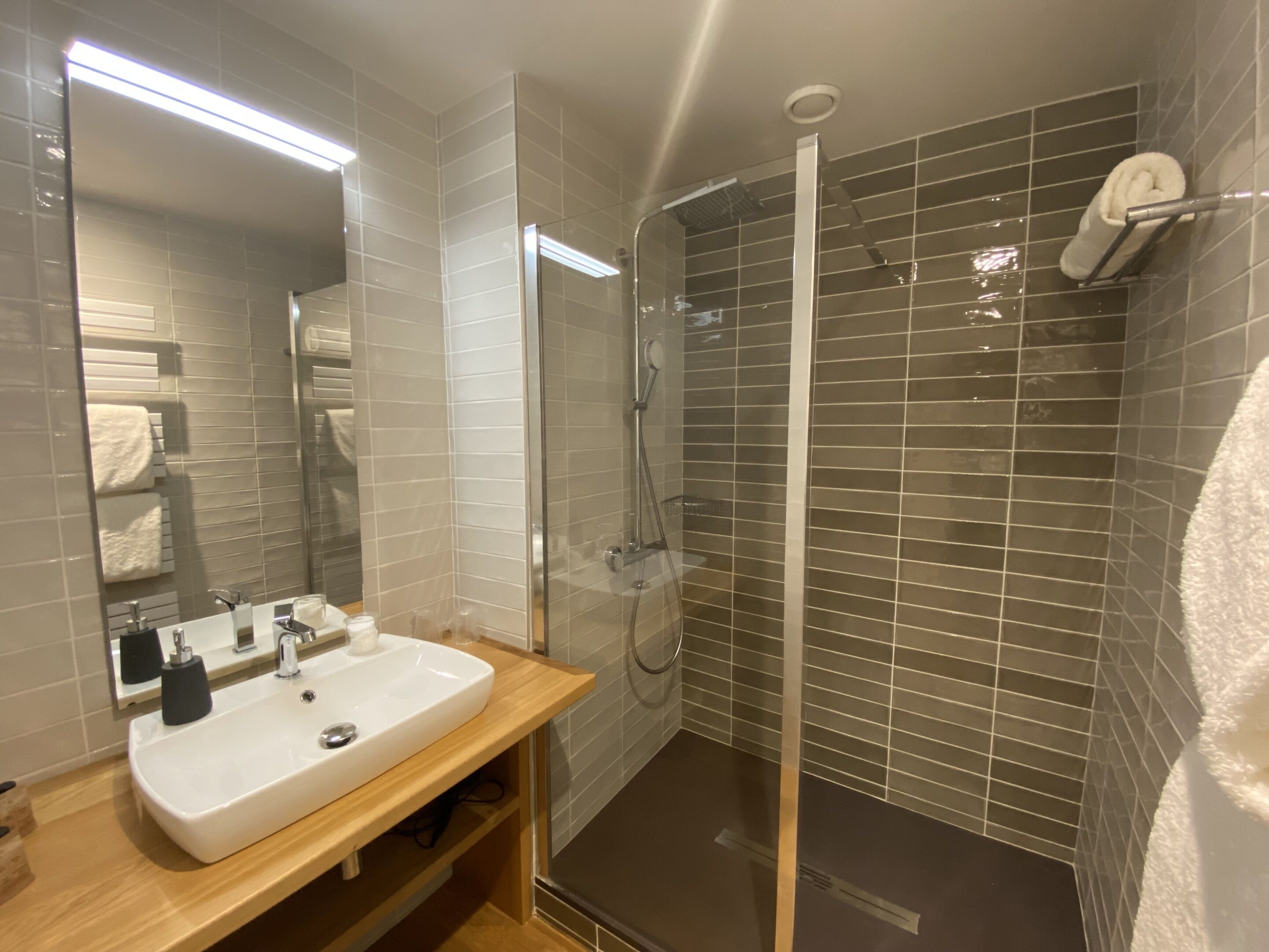 Une salle de bain moderne avec un lavabo blanc, un miroir et un espace douche.