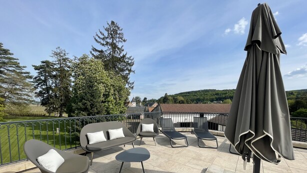A terrace with outdoor seating, a table, and a large umbrella. - Manoir de Villamont (Savigny-les-Beaune)