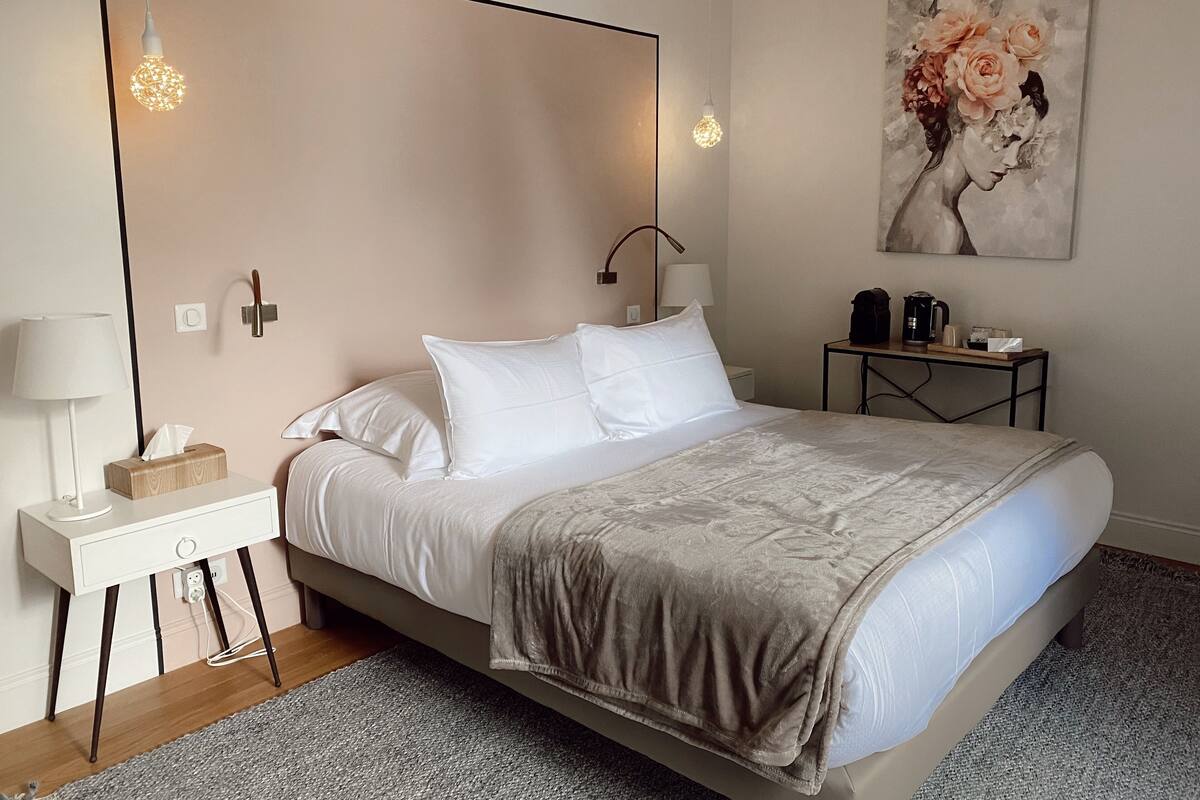 A neatly arranged bedroom with a large bed, bedside tables, a lamp, and a painting on the wall.