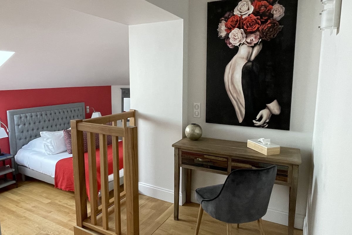 A bedroom with a bed, a desk, a chair, and a painting on the wall.