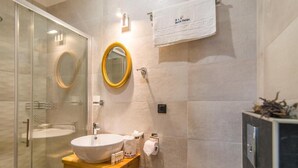 A bathroom with a glass-enclosed shower, a round mirror, a wooden vanity with a white sink, and a towel rack with a branded towel. - BELLA NATKA BED AND BREAKFAST (Rovinj)