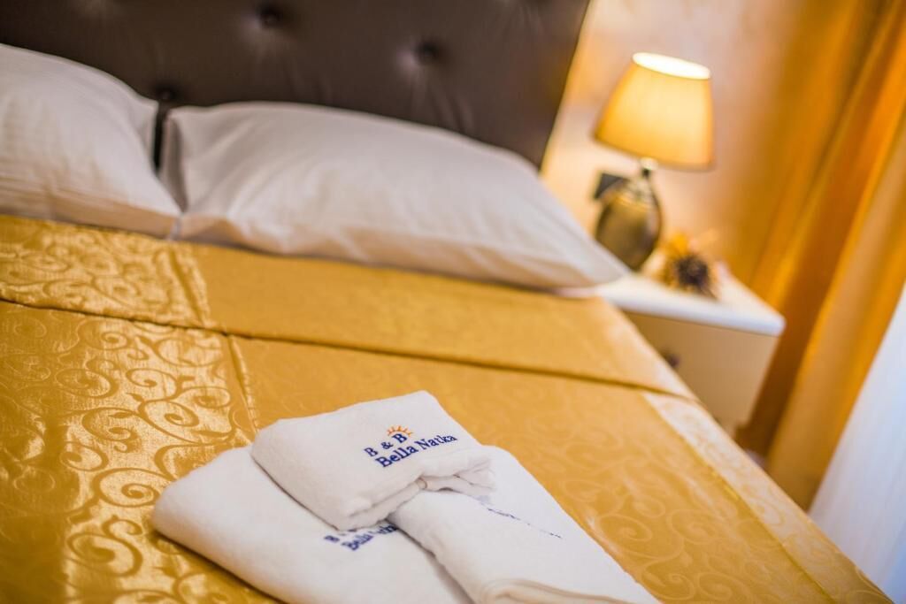 A neatly made bed with a folded towel and a lamp on a bedside table.