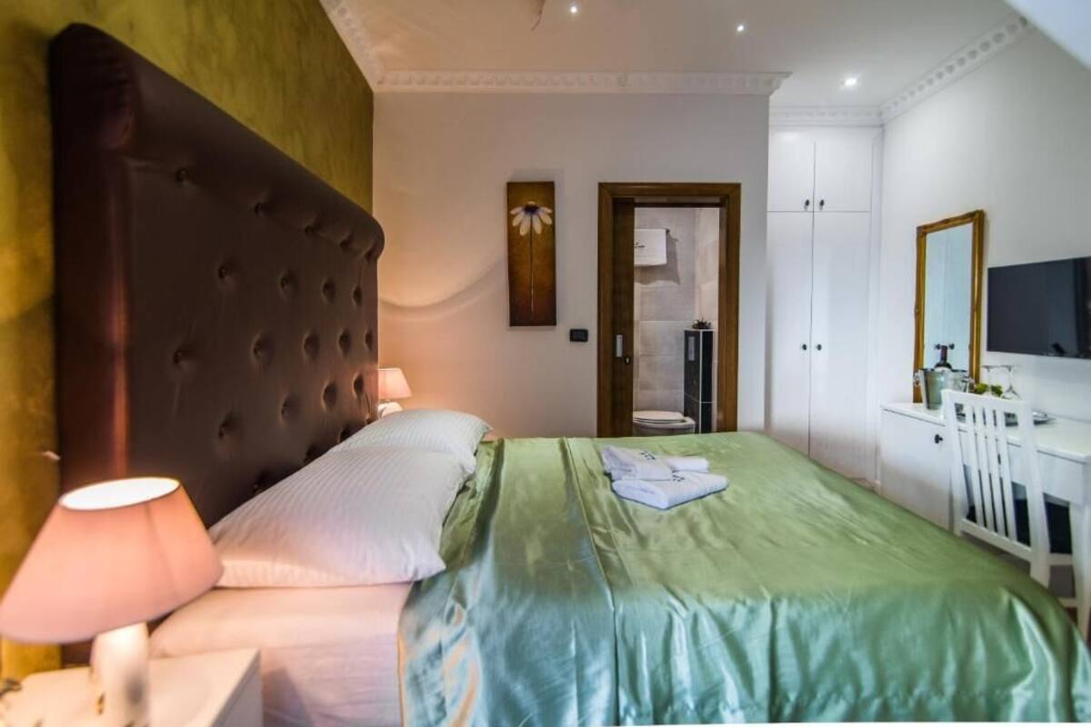 A hotel room with a large bed, a bedside lamp, a wardrobe, a desk with a chair, and a television.