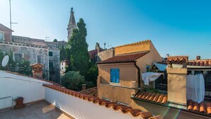 A rooftop terrace with terracotta tiles, a white railing, and a view of surrounding buildings and a church tower. - BELLA NATKA BED AND BREAKFAST (Rovinj)